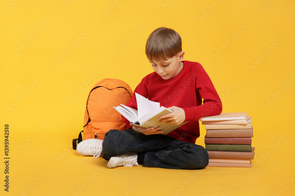 Cute schoolboy with backpack reading book on orange background Cute schoolboy with backpack reading book on orange background
