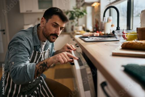Fotografie Mid adult man using dishwasher while doing the dishes in the kitchen