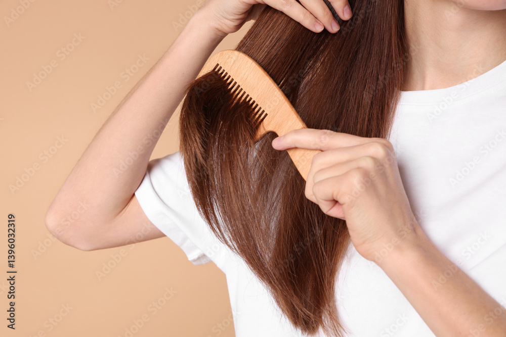 Fototapeta premium Woman brushing her hair with comb on beige background, closeup