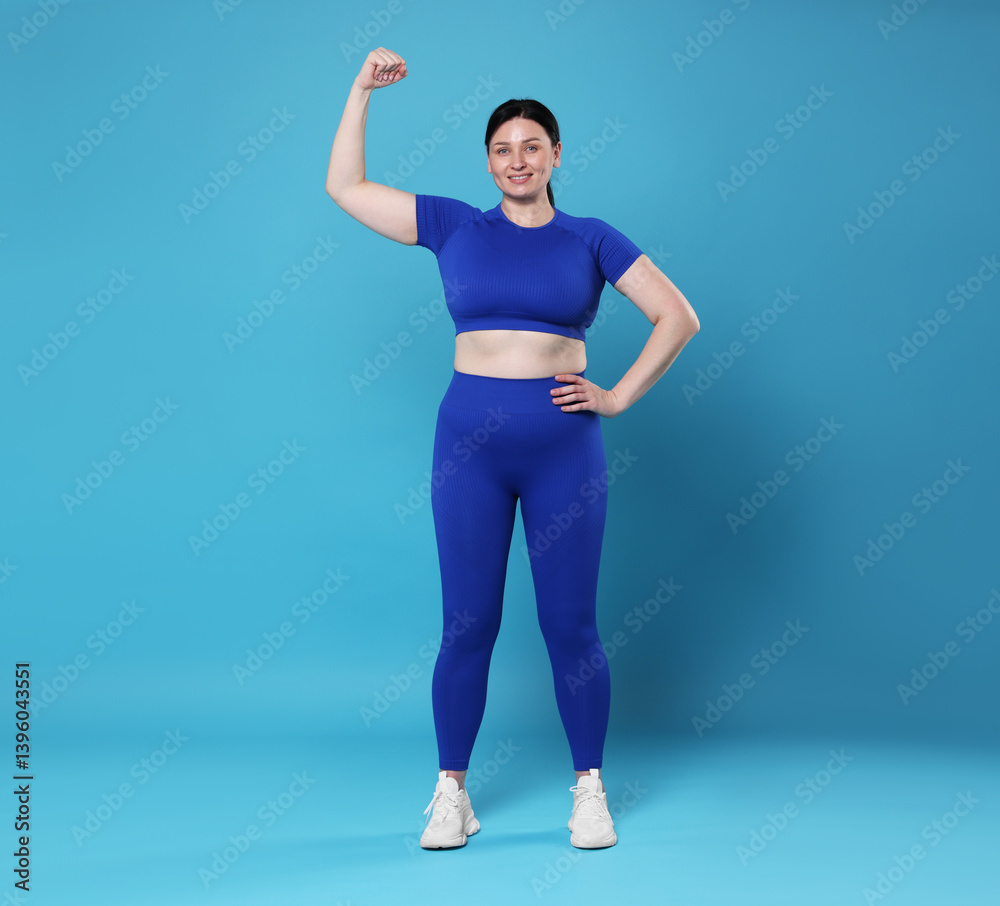 Obraz premium Plus size woman in gym clothes showing her bicep on light blue background, space for text