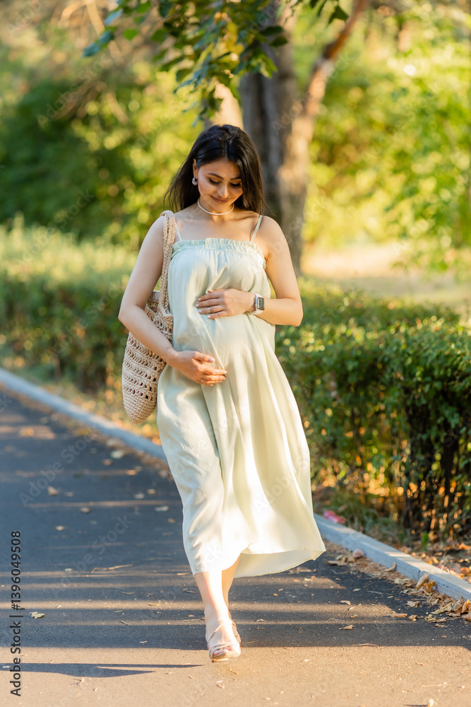 Beautiful brunette pregnant woman walks in the park at sunset in summer Beautiful brunette pregnant woman walks in the park at sunset in summer