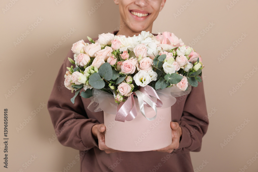 Smiling delivery man holding gift box with beautiful floral composition on beige background, closeup Smiling delivery man holding gift box with beautiful floral composition on beige background, closeup