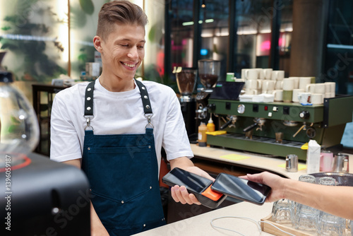 Cafe worker taking payment from client via terminal indoors