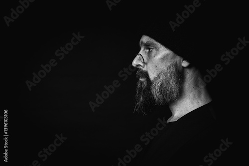Obraz na płótnie black and white, portrait, expressive mature man with sharp gaze and frowning face, wearing glasses and knitted hat, looking aside. Dramatic portrait with strong emotions on dark background, gaze. w salonie
