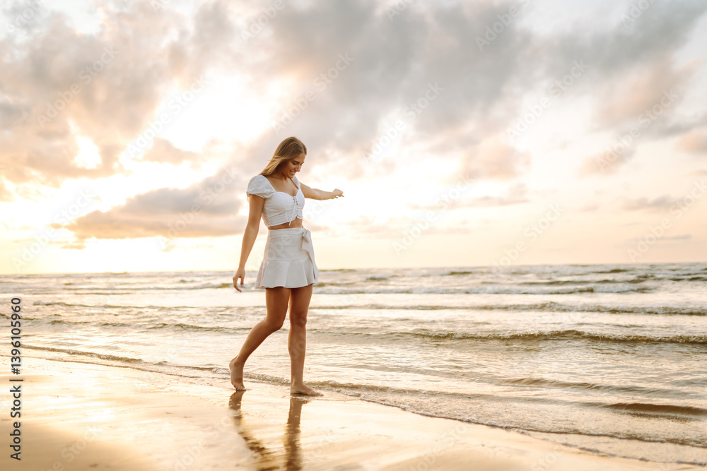 Happy young woman walking on sandy beach at sunset. Smiling woman enjoying weather and feeling freedom outdoors. Vacation, weekend concept. Lifestyle. Happy young woman walking on sandy beach at sunset. Smiling woman enjoying weather and feeling freedom outdoors. Vacation, weekend concept. Lifestyle.