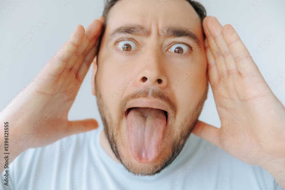 Man expresses shock with raised hands and playful tongue gesture indoors Man expresses shock with raised hands and playful tongue gesture indoors