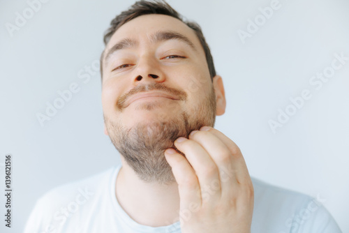 Man grooming his beard while smiling in a bright indoor setting