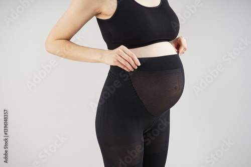 Young pregnant woman in black tights on grey background
