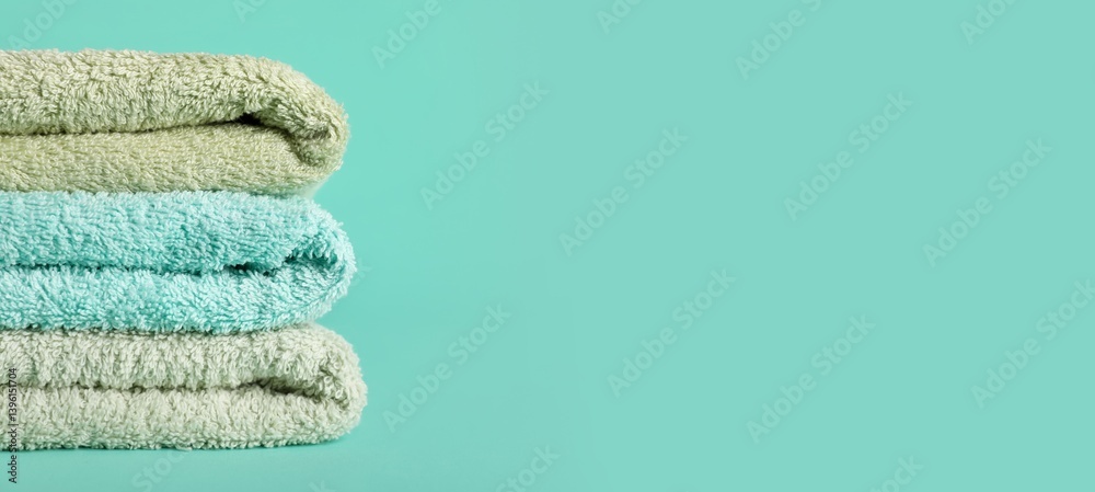 Stack of clean soft towels on turquoise background with space for text, closeup