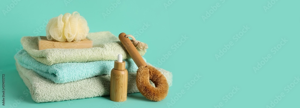 Stack of clean towels, bath sponge, brush and shampoo on turquoise background with space for text