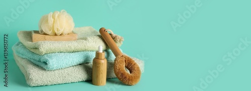 Stack of clean towels, bath sponge, brush and shampoo on turquoise background with space for text