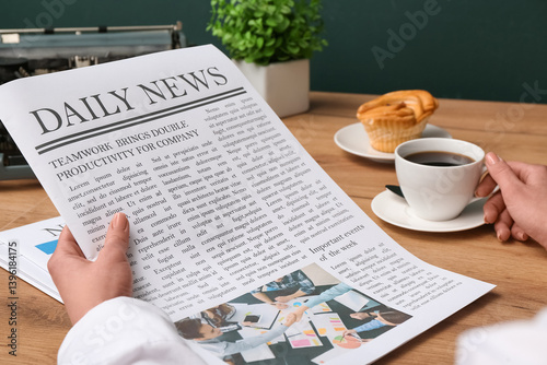 Female hands holding cup of coffee and newspapers on wooden table