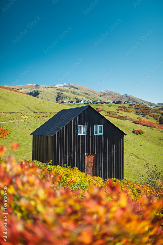 Dark wooden cabin stands on a grassy hillside, surrounded by fall foliage and mountains, Gomis Mta, Georgia