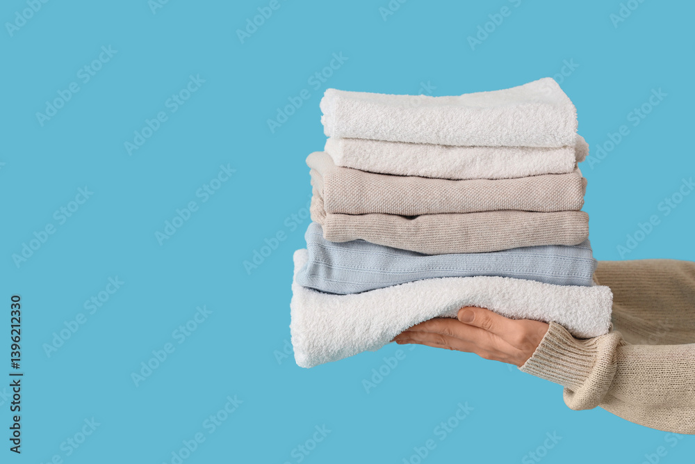 Female hands with stack of stylish clothes and towels on blue background, closeup