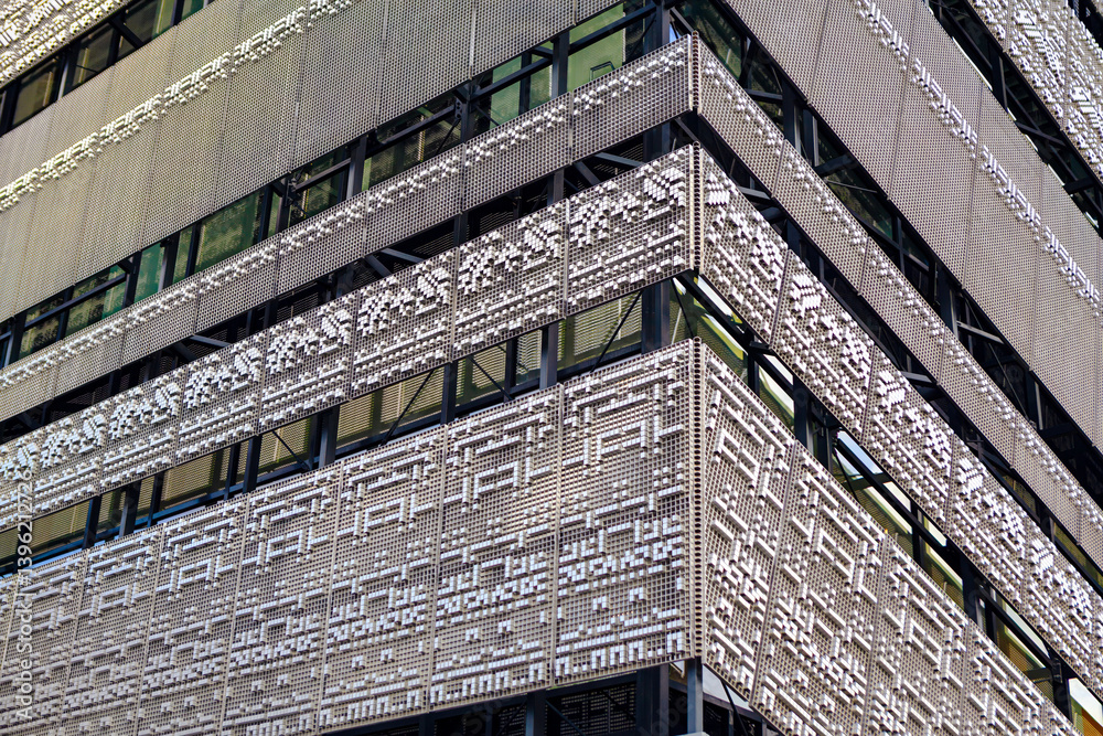 Modern building facade features intricate, perforated metal panels with geometric patterns, reflecting urban sophistication. Sleek design with large windows captures contemporary architecture