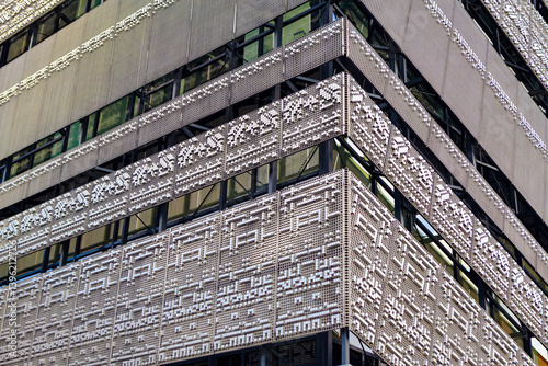 Obraz na płótnie Modern building facade features intricate, perforated metal panels with geometric patterns, reflecting urban sophistication. Sleek design with large windows captures contemporary architecture w salonie
