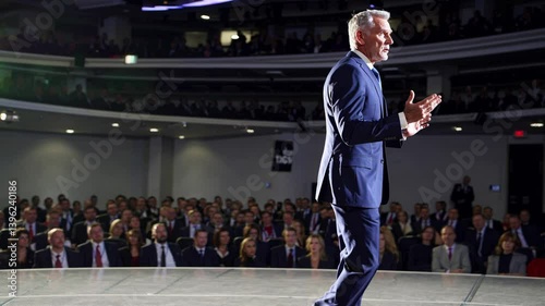 Confident businessman delivering inspiring keynote speech to large audience in modern auditorium