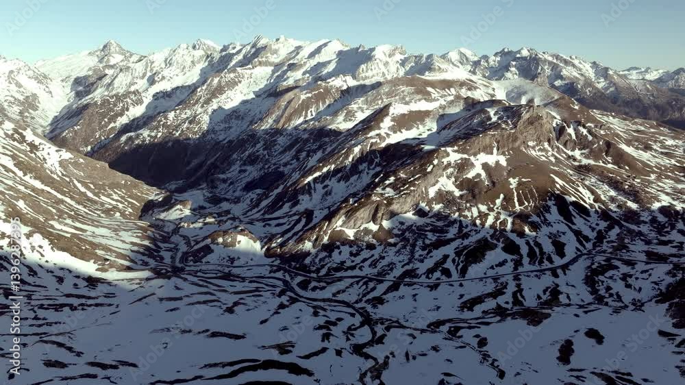 Aerial shot - Soft sunlight gradually revealing snow covered mountain peaks and shadowy valleys in Pyrenees National Park, spanning Spanish French border with breathtaking natural beauty