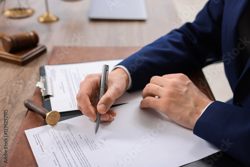 Notary signing document at wooden table in office, closeup photo