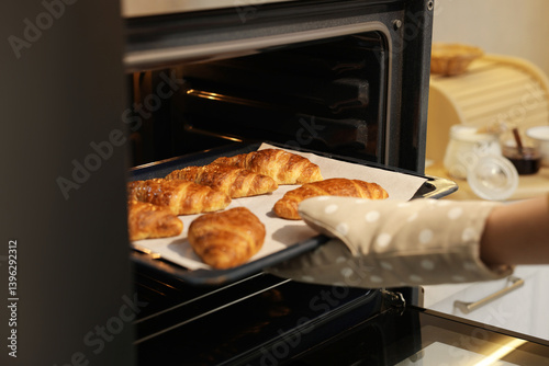 Schilderij op canvas Woman taking baking sheet with tasty croissants out of oven indoors, closeup