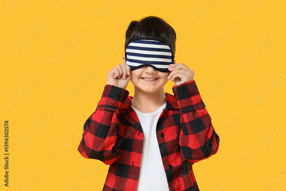 Cute boy in pajamas with sleeping mask on yellow background Cute boy in pajamas with sleeping mask on yellow background