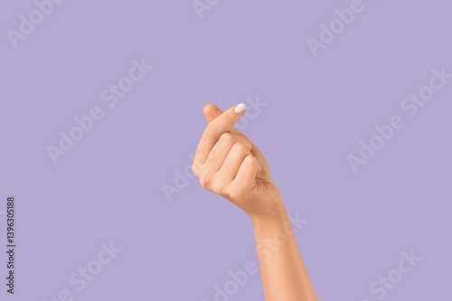 Female hand making heart gesture on lilac background