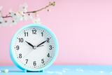 Alarm clock and blooming branch on pink background. Spring time