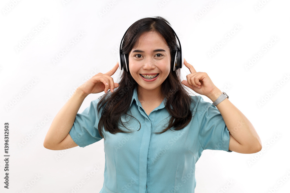 Cropped photo of dark-haired smiling woman touching headphones with index fingers and looking at camera on white background. Human emotions and face expressions concept Cropped photo of dark-haired smiling woman touching headphones with index fingers and looking at camera on white background. Human emotions and face expressions concept