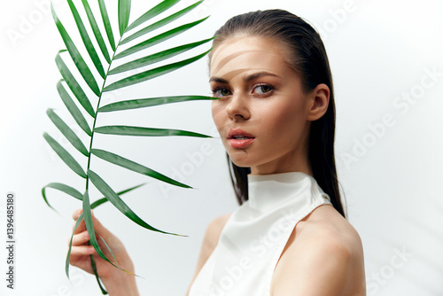 Elegant model holding a palm leaf, showcasing natural beauty with a minimalist background, exuding serenity and style in soft lighting.