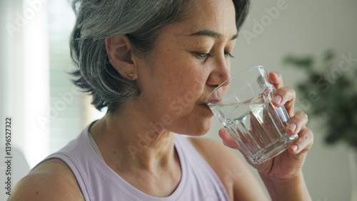 Photos Asia adult people middle age happy old woman smile look at camera drink water stay hydrated reduce hot flash dry skin health care sit at home sofa elder aging asian aged female