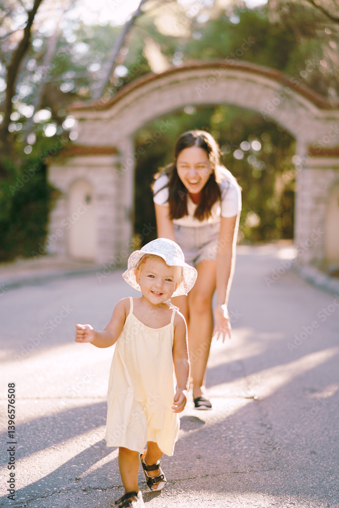 Naklejka premium Laughing mom chasing little girl down the road in the park