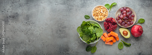 Assortment of healthy potassium rich foods including cashews, grapes, avocado, pomegranate, baby carrot and spinach placed on a gray background, a balanced diet for wellness