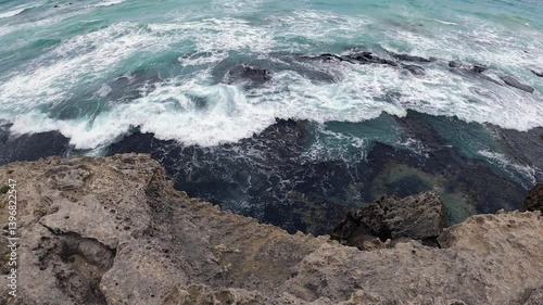 Waves in turquoise sea crash onto shoreline limestone reef, copy space