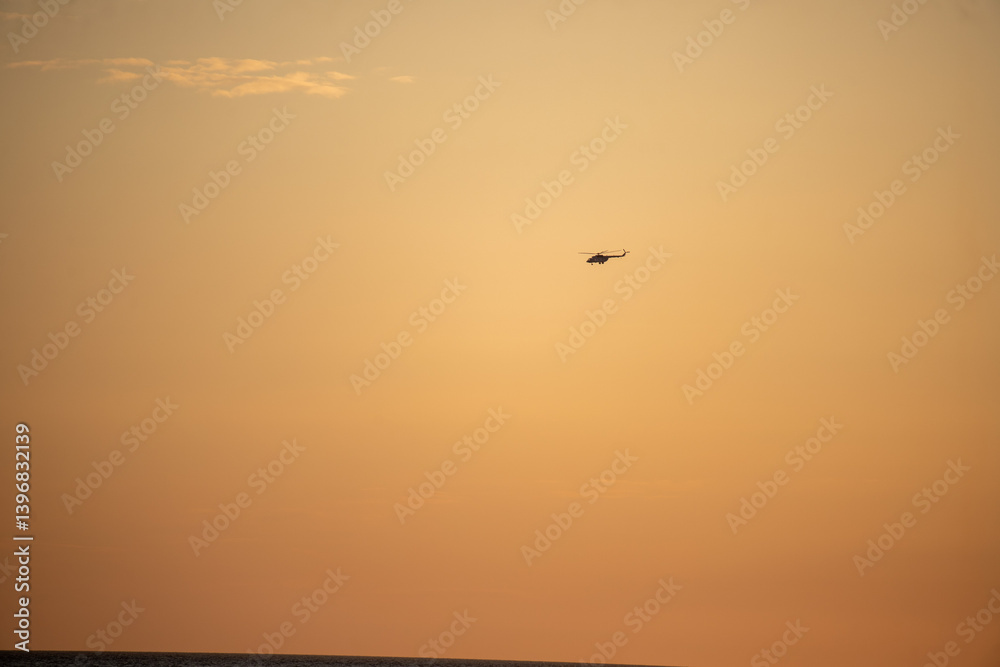 A helicopter flies over a beautiful orange sky A helicopter flies over a beautiful orange sky