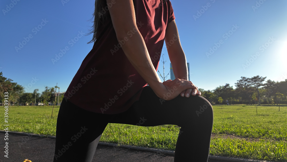 Young woman stretching after exercise and jogging in urban park during sunny summertime day..