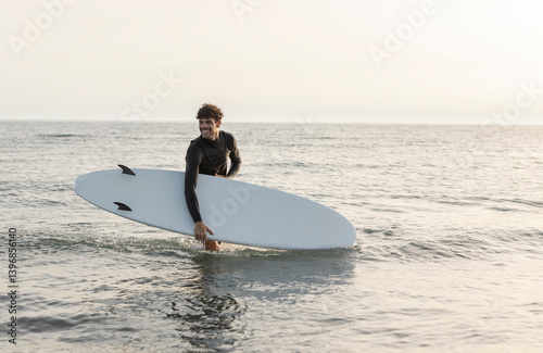 Surfer carrying surfboard in ocean at sunset