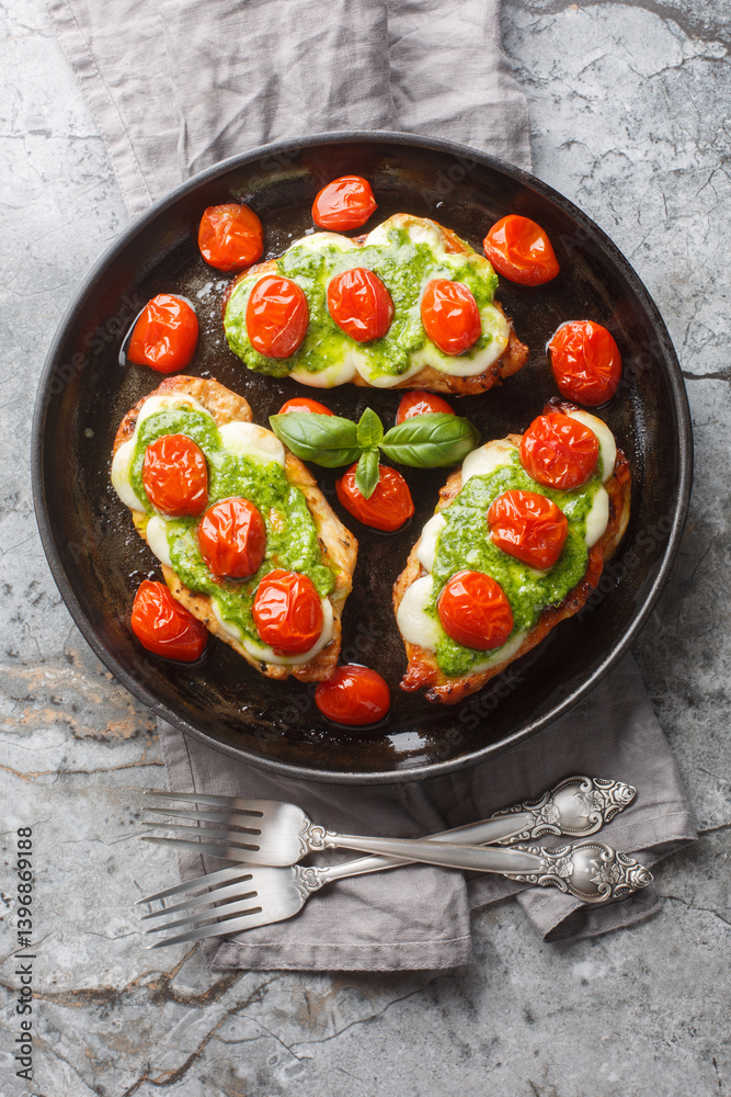 Grilled chicken margherita topped with melted mozzarella cheese, basil pesto and tomato close-up on pan on table. Vertical top view from above