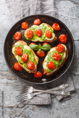 Obraz na płótnie Grilled chicken margherita topped with melted mozzarella cheese, basil pesto and tomato close-up on pan on table. Vertical top view from above w salonie