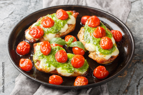 Chicken margherita is made with juicy pan-seared chicken, topped with basil pesto, mozzarella, roasted cherry tomatoes close-up on pan on table. Horizontal