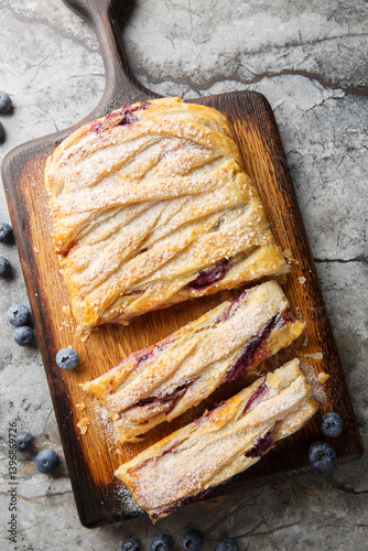 Puff pastry pie with blueberries and cream cheese close-up on wooden board on table. Vertical top view from above
