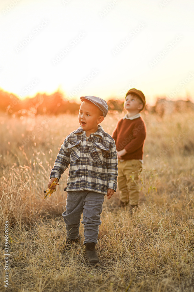 Two little boys in flat caps playing together in a golden field at sunset. Vintage rural scene, capturing the essence of childhood innocence, freedom, and nature. Two little boys in flat caps playing together in a golden field at sunset. Vintage rural scene, capturing the essence of childhood innocence, freedom, and nature.