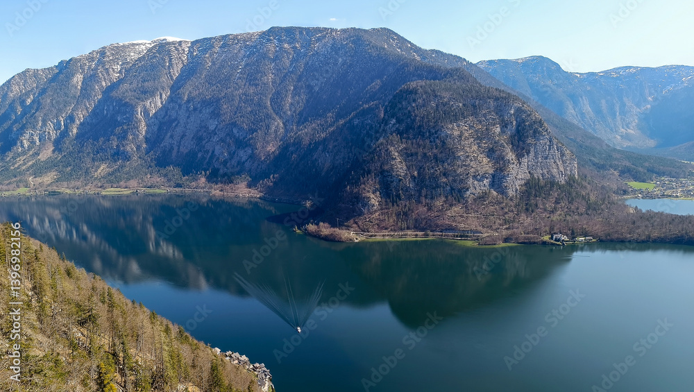 Obraz premium Mountain lake surrounded by forest and rocky cliffs with boat sailing on water surface.