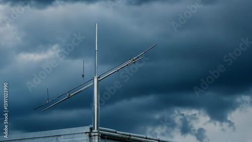 High metal communications antenna on a rooftop silhouetted against a dramatic sky with heavy storm clouds gathering on the horizon