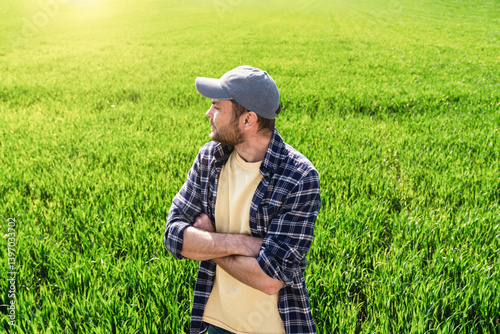 Male farmer agriculturalist with crossed arms standing in a winter wheat field in early spring