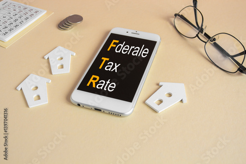 Concept words Federal tax rates on the mobile phone screen. Beautiful beige background. Glasses, miniature houses, coins. Business concept.