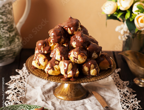 Profiterole cake, or cream puff, is a French choux pastry ball filled with whipped cream, custard, and chocolate sauce, served on a gold plate.