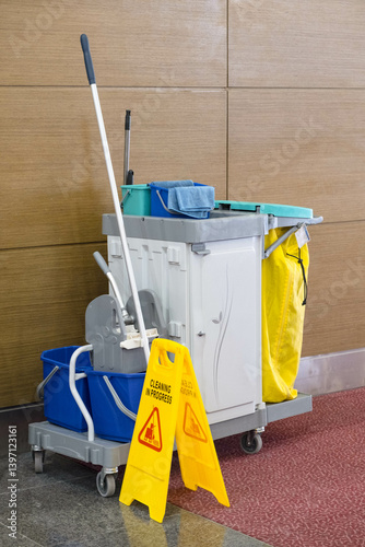 Fotografie Cleaning cart with mop, bucket, and cloths stands in a hallway alongside a Cleaning in Progress sign