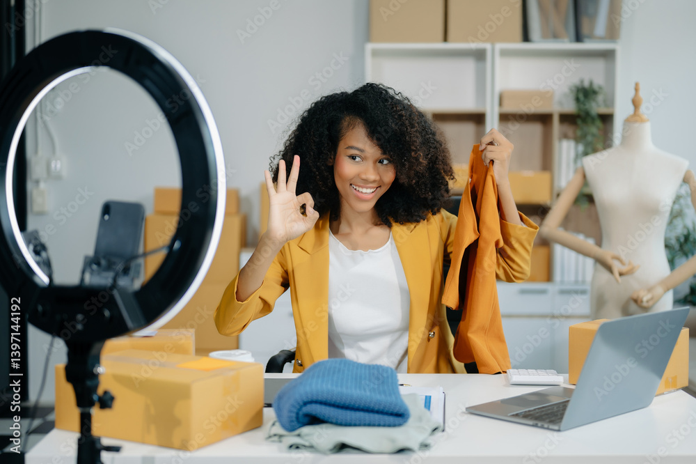 Beautiful lady blogger showing clothes in front of the camera to recording vlog video live streaming at her shop