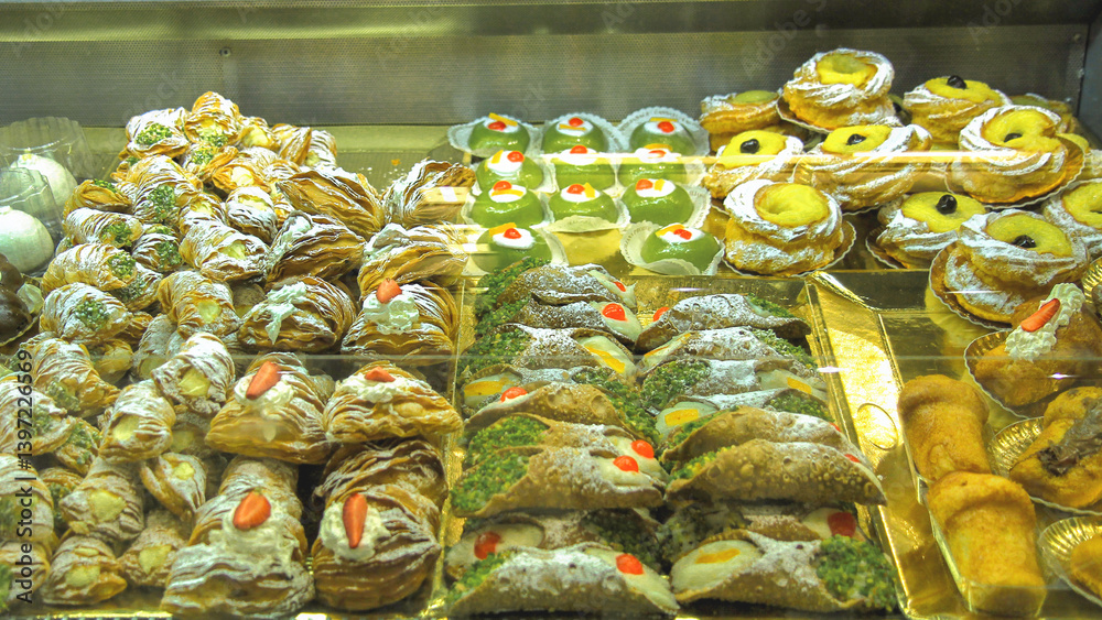 Display of Italian pastries with cannoli and sfogliatella in a bakery window.