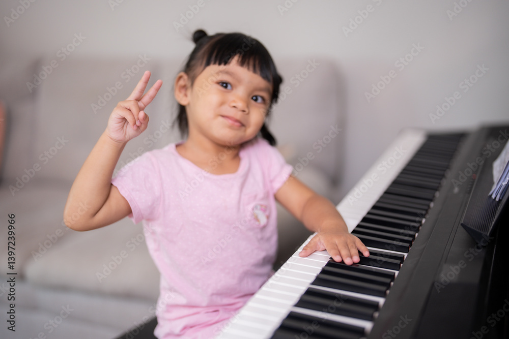 Young Asian girl enjoy plays piano at home. Little kid prcatices music instrument in house. Child interested in musical riased two finger and smile. Young Asian girl enjoy plays piano at home. Little kid prcatices music instrument in house. Child interested in musical riased two finger and smile.